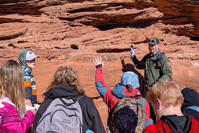 uniformed ranger stands with students before reddish sandstone cliff
