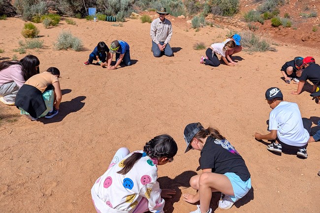 students in pairs build mounds in open sandy field with ranger observing