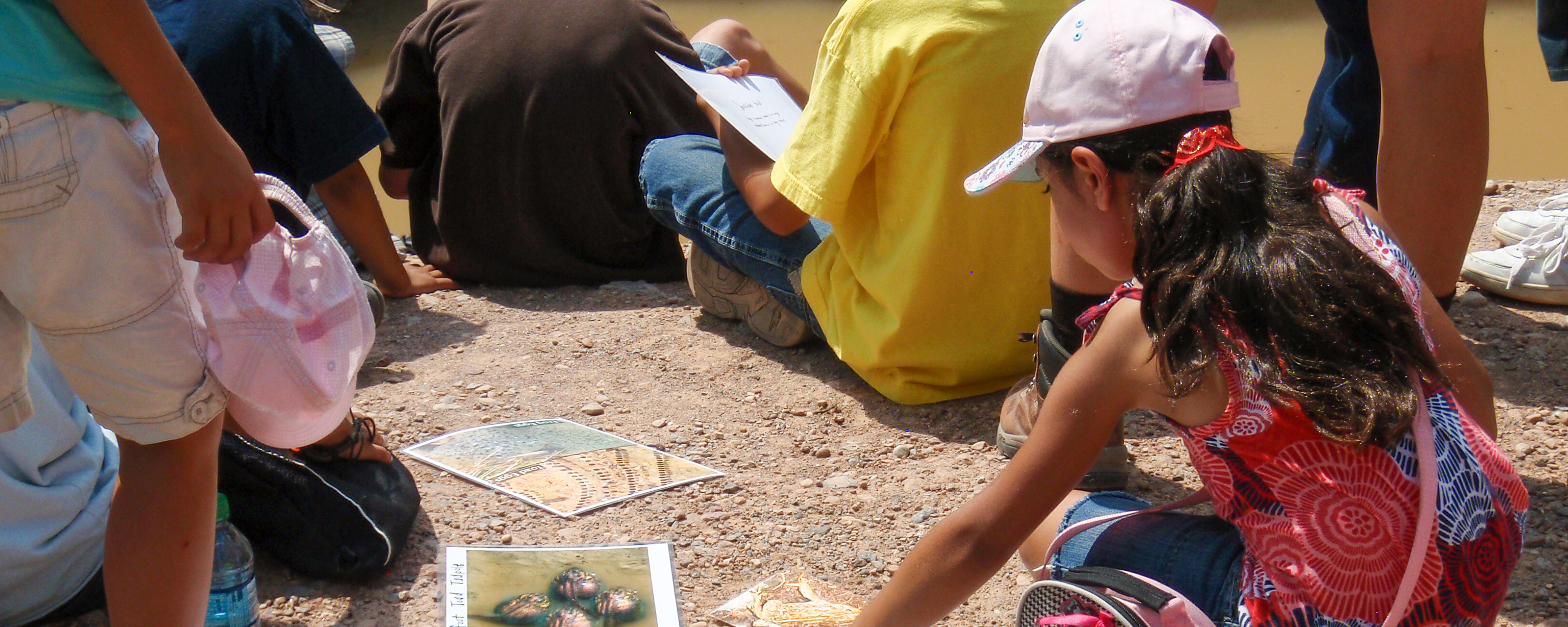 a young girl in a pink outfit reaches down to laminated guides, surrounded by other young people
