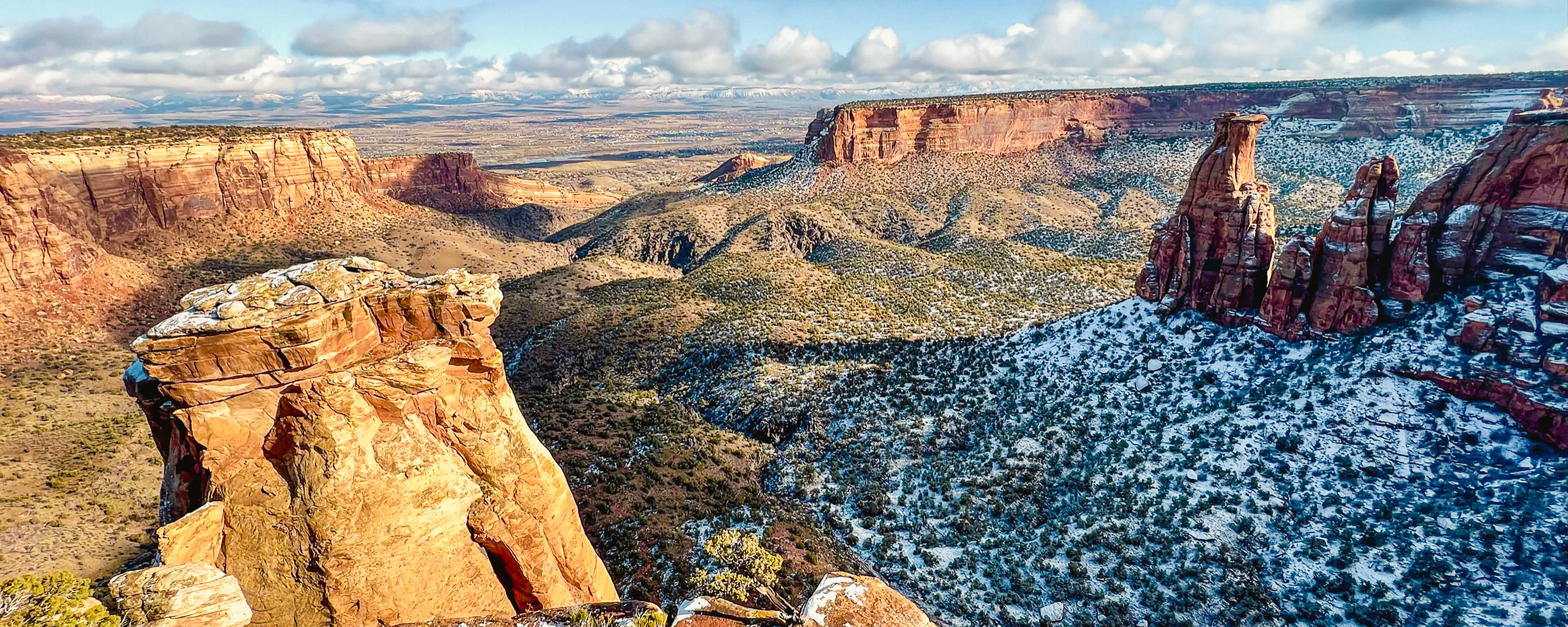 red-rock cliffs frame rolling green canyon bottoms, snow in shade below