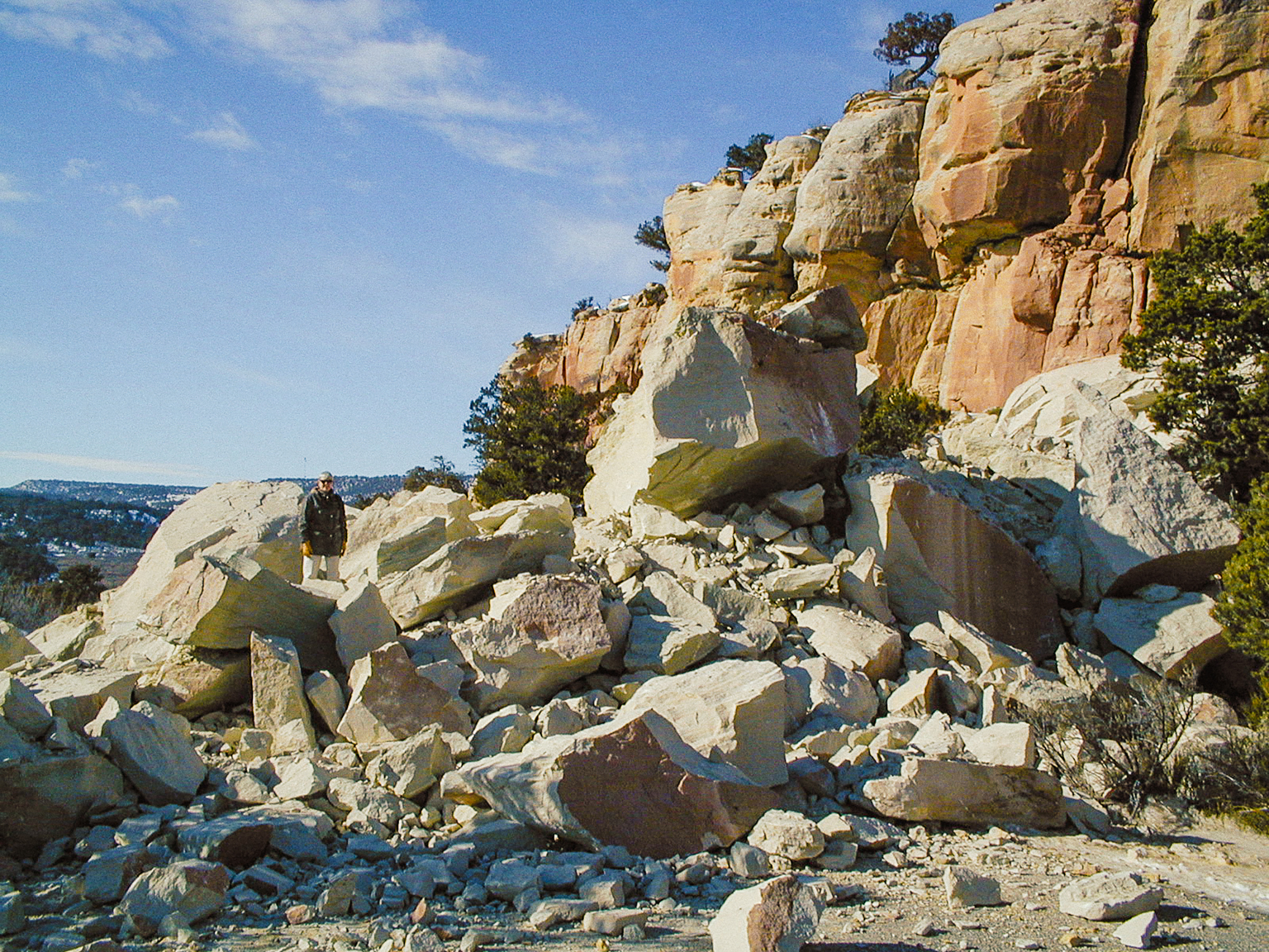 Person stands comparatively small by enormous pile of boulders.