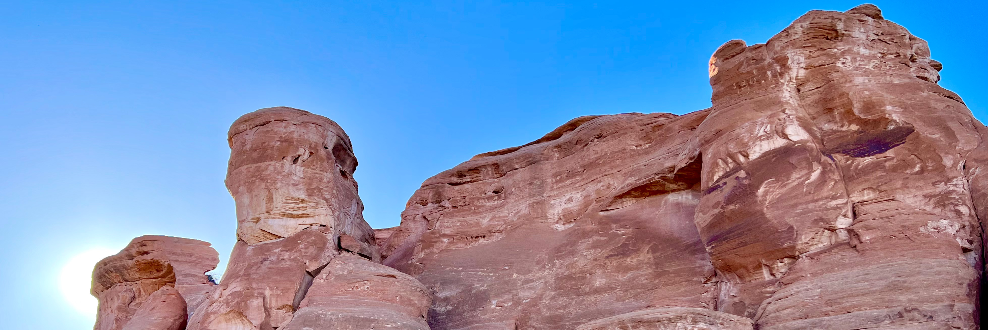sunlight peeks from behind salmon colored sandstone shapes of Saddlehorn rock formation