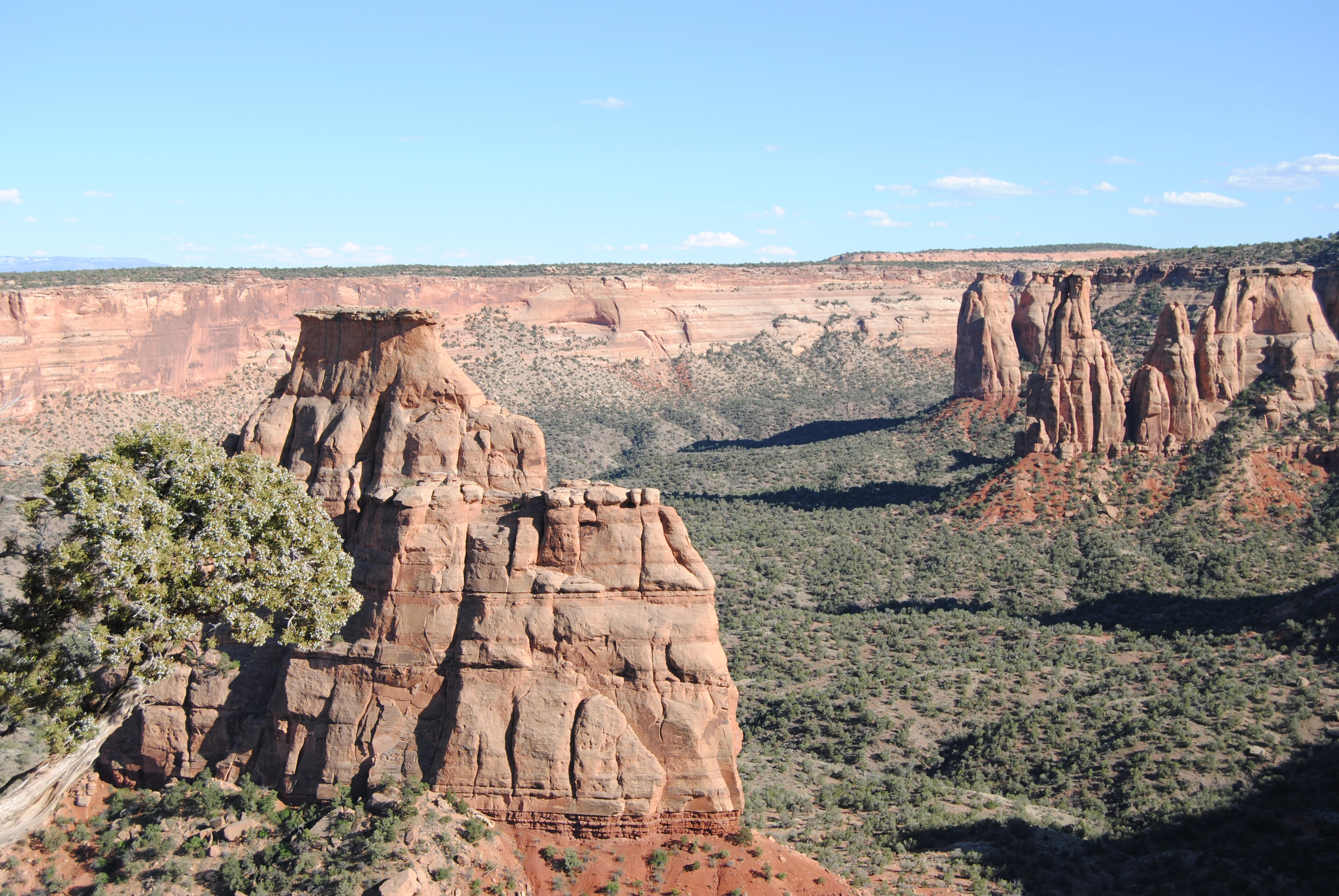 Large rock monolith within a wide canyon. In the background along the canyon wall are other rock monoliths.