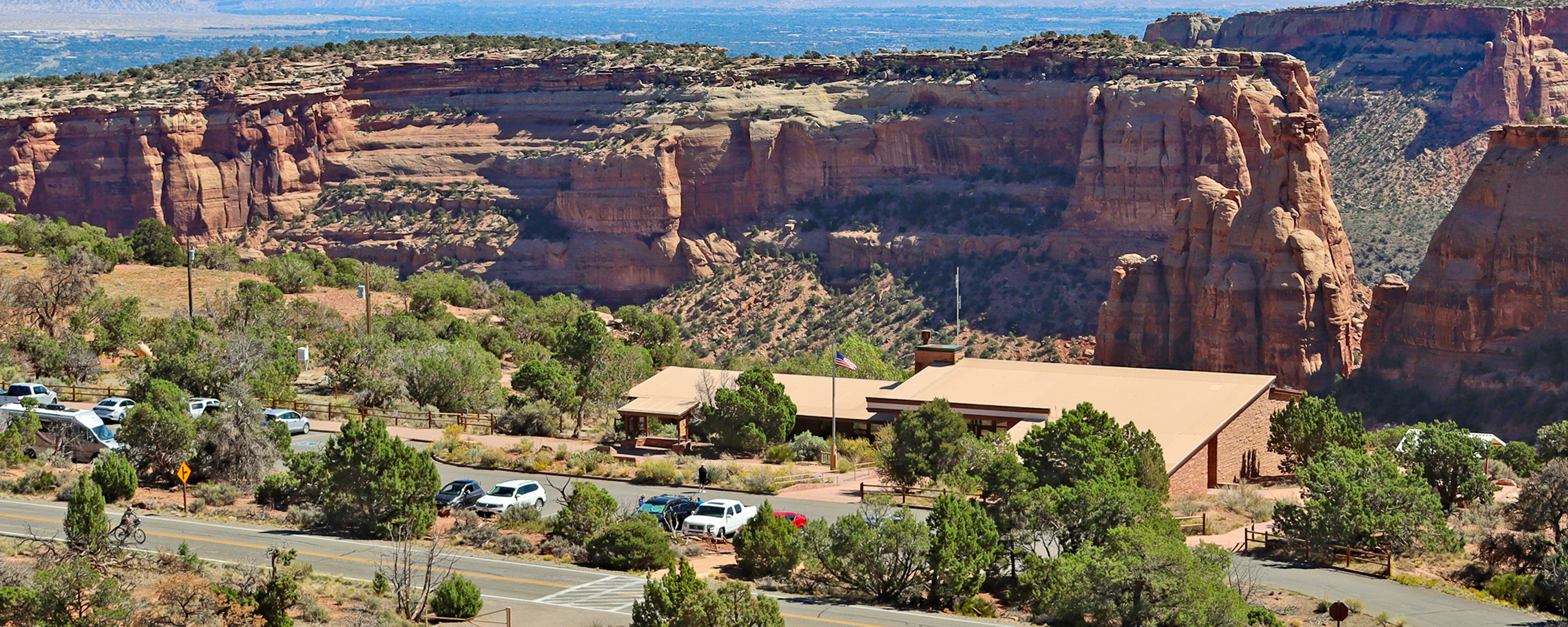 a flat roofed building surrounded by low growing trees stands on the edge of a canyon
