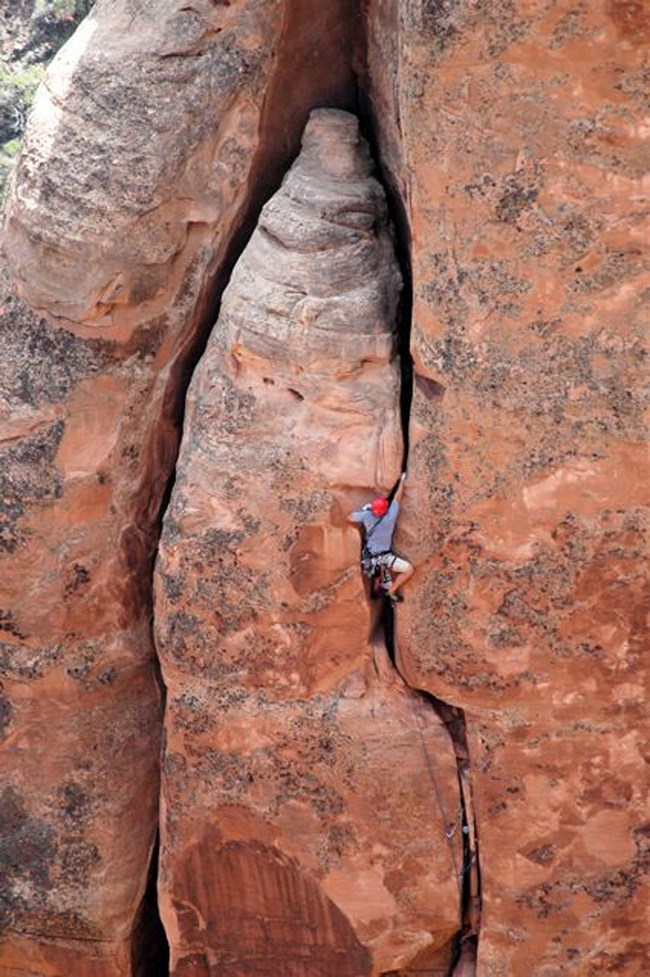 Climber in a red helmet ascends a sandstone cliff crack in Colorado National Monument.
