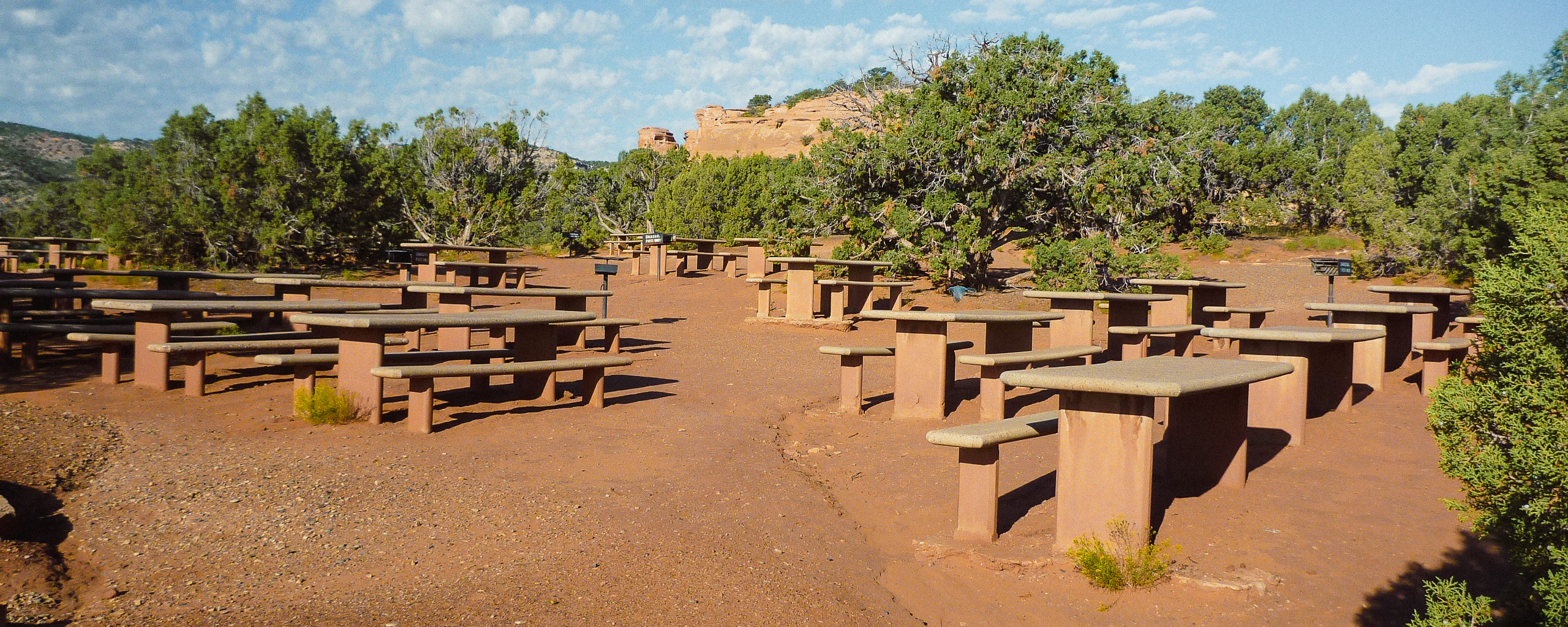 stone picnic tables spread across reddish sand surrounded by green juniper trees