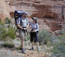 Two hikers wearing sun hats and a baby riding in a backpack carrier, with a sun shield for protection.