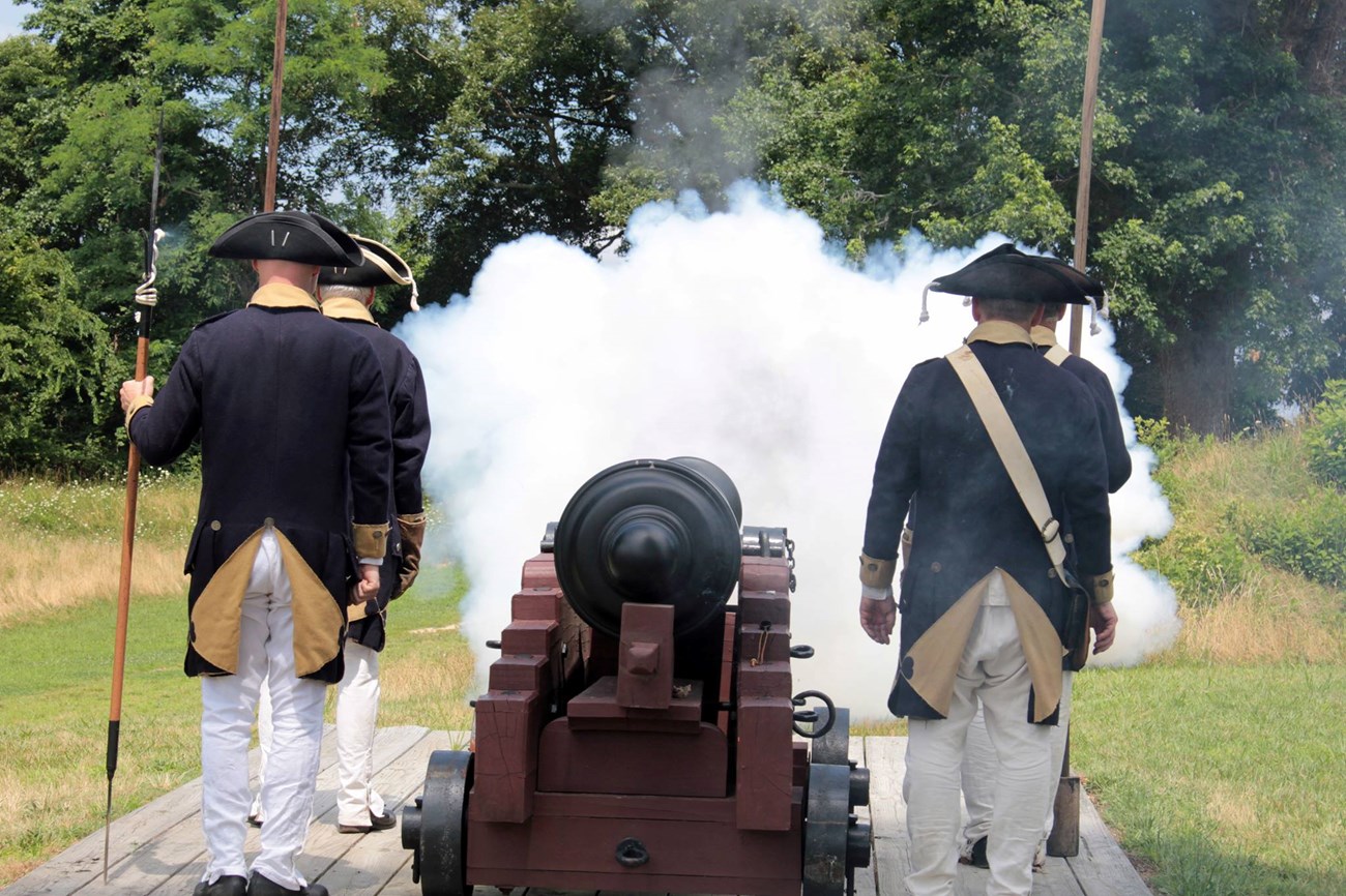 Reenactors fire a cannon at Yorktown battlefield. They wear continental army uniforms.