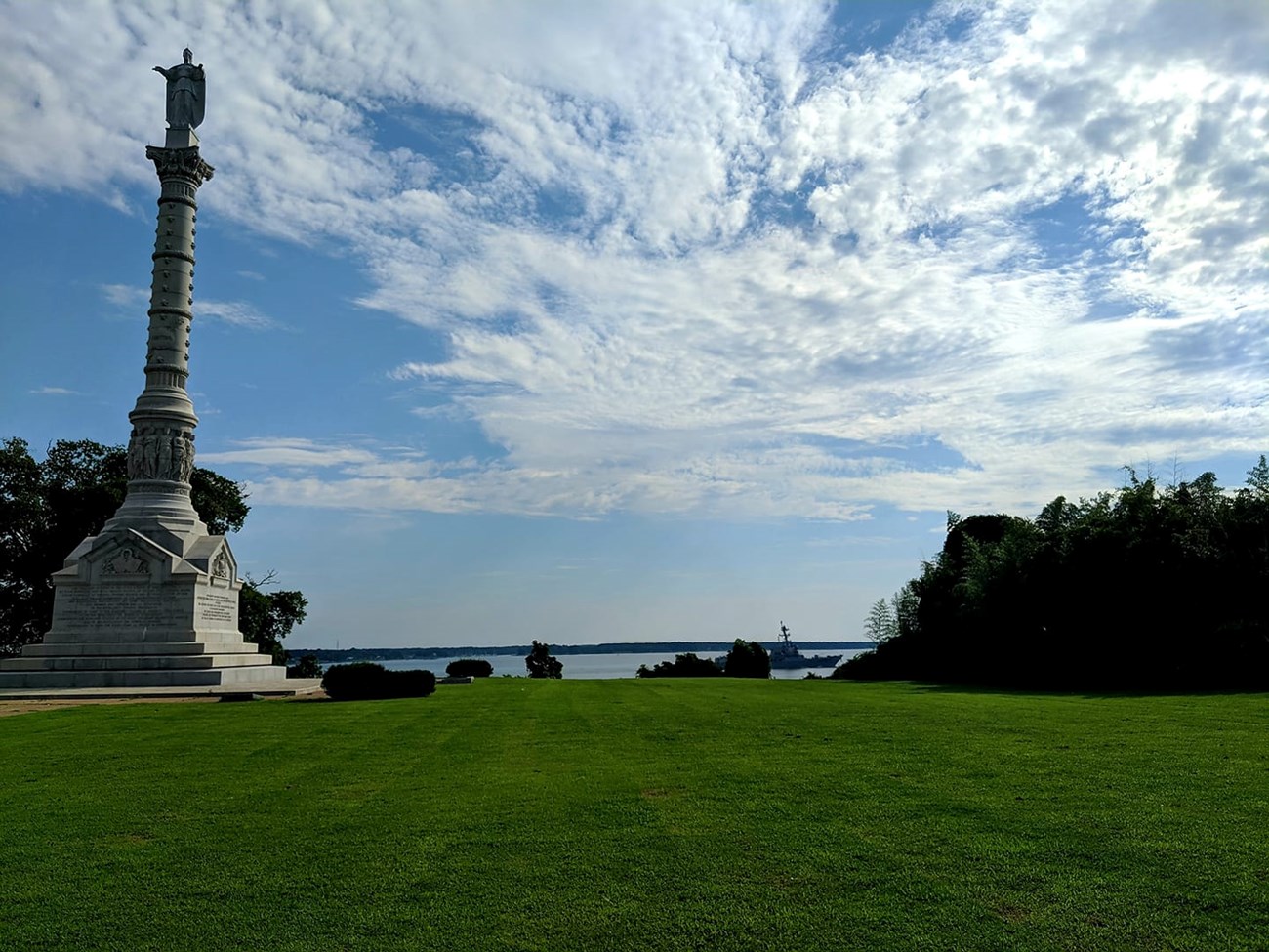 A tall obelisk monument is pictures in front of a blue cloudy sky. In the background is the York River.