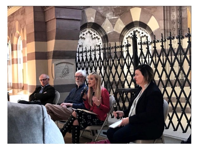 four people sitting on chairs one holds a microphone and is speaking