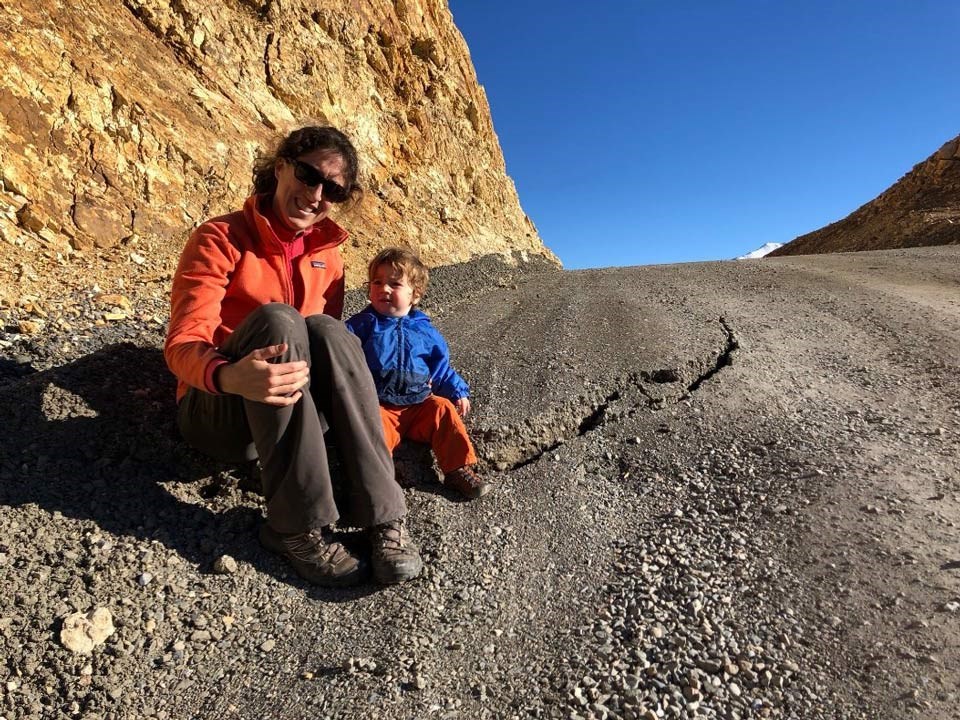 woman and child sitting on a dirt road with a large crack in the middle of it