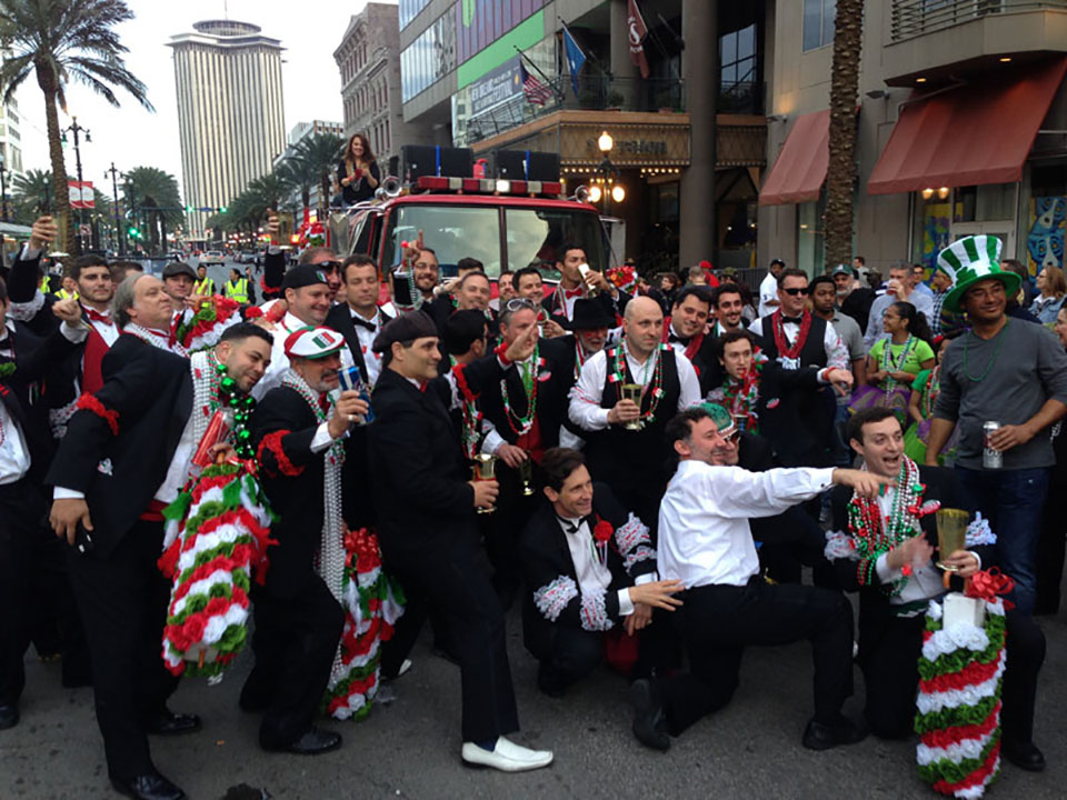 marching band and other dressed in green, orange and white silk clothes carrying banners down a street