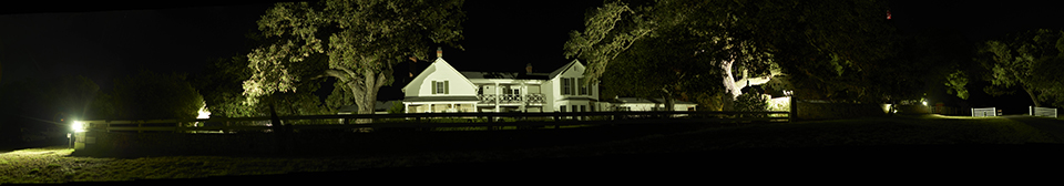 A large, two-story white house glows at night from exterior lighting.