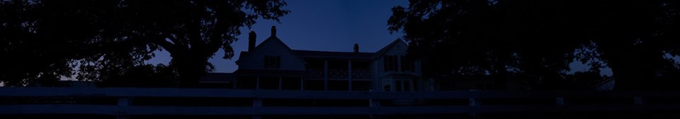 A large, two-story white house glows at night from exterior lighting.