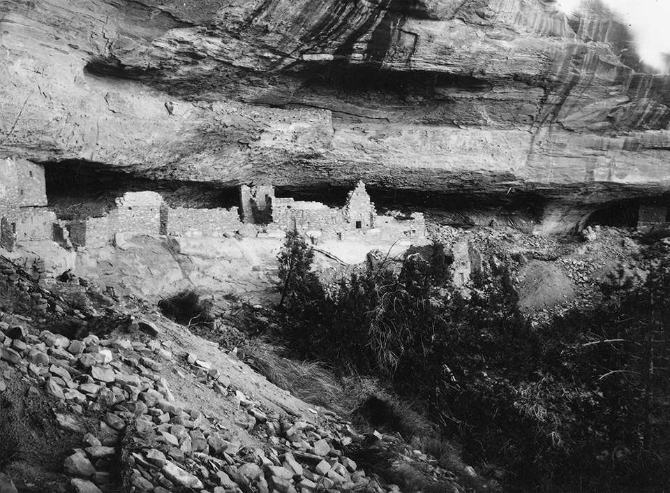 Ancient, stone-masonry village rooms under an alcove with crumbled walls and piles of rubble.