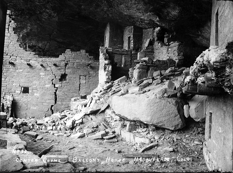 Ancient, stone-masonry village rooms under an alcove with crumbled walls and piles of rubble.