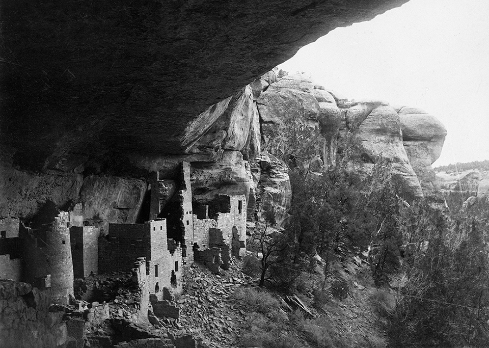 Ancient, stone-masonry village rooms under an alcove with crumbled walls and piles of rubble.
