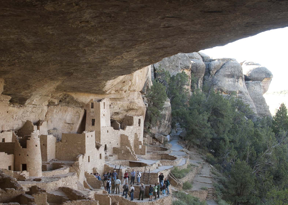 Ancient, stone-masonry village rooms under an alcove with crumbled walls and piles of rubble.