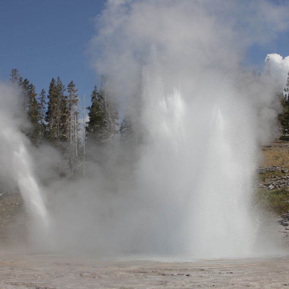 Steam and water erupt out of a beehive-shaped cone of rock.