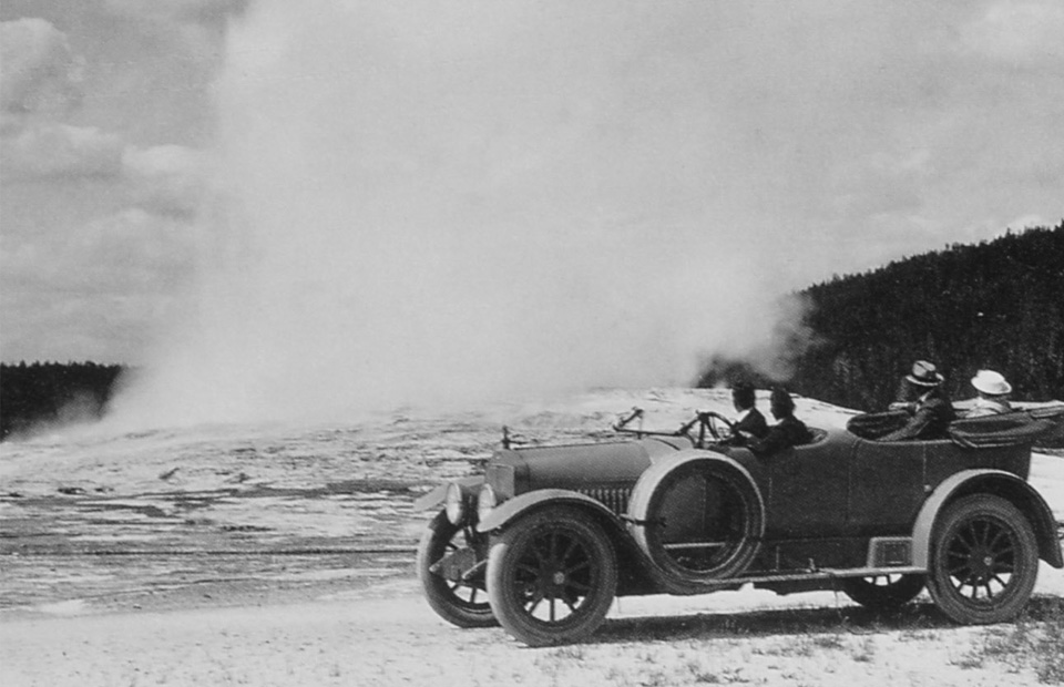 People stand on a boardwalk and watch steam and water gush into the air.