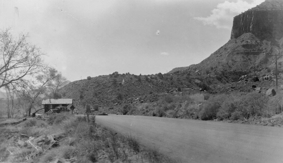 Black and white photo of the South Entrance with a road and structure and cliffs in the background.