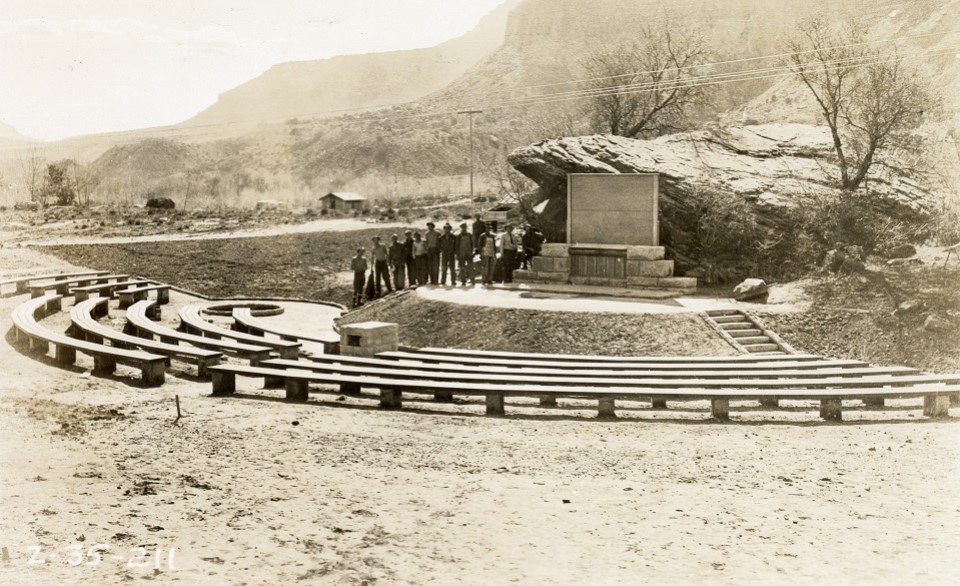 Black and white photo of rows of benches in front of a small screen with Zion Canyon in the background.