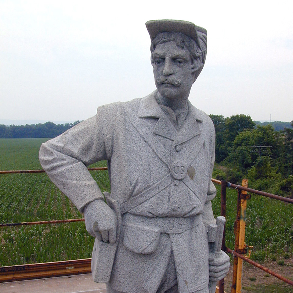 Granite statue of a Union soldier with dark specks of lichen on it. The stone appears dark gray.