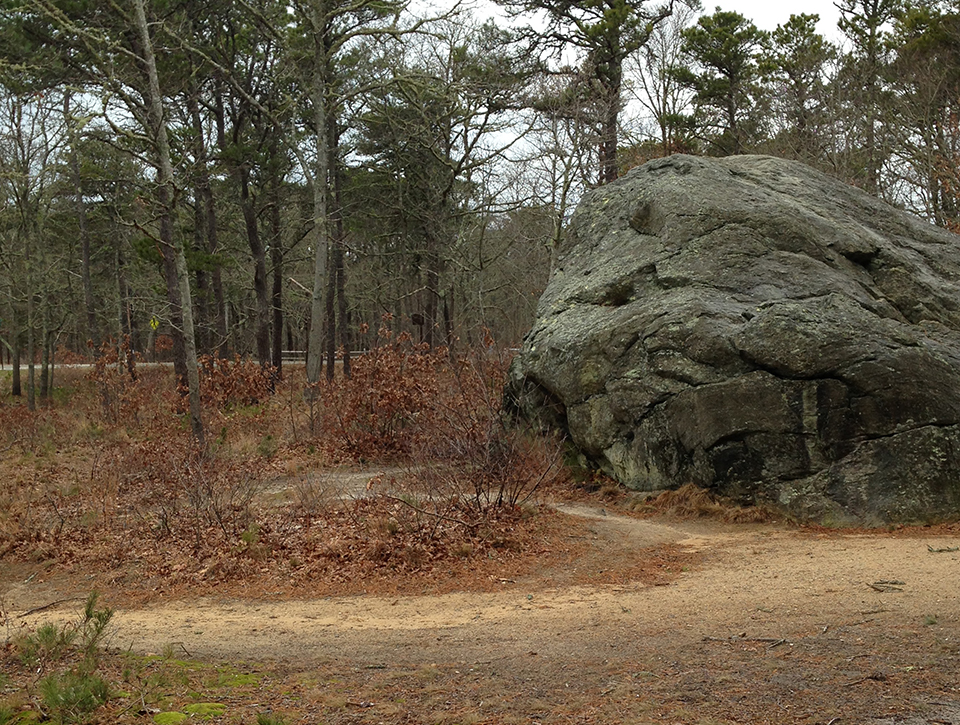 A black and white photo of three people sitting on a large boulder in an open field.