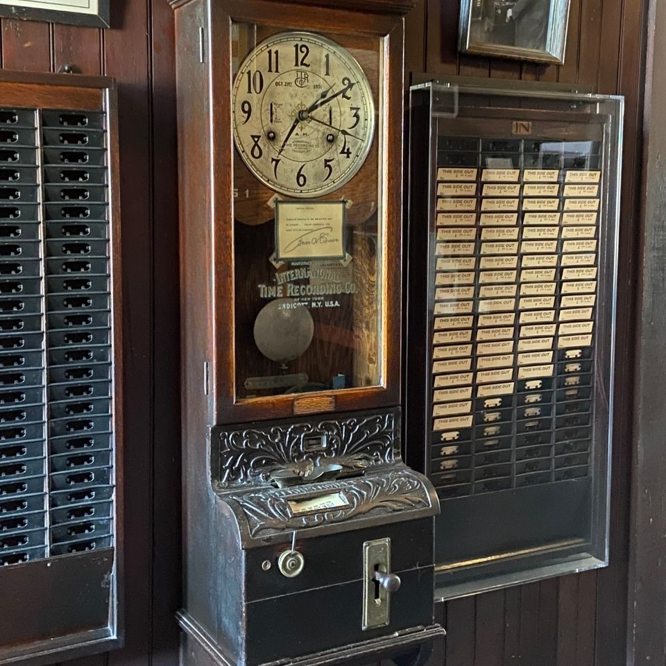Black and white photo of Thomas Edison punching in at time clock, time cards to the left