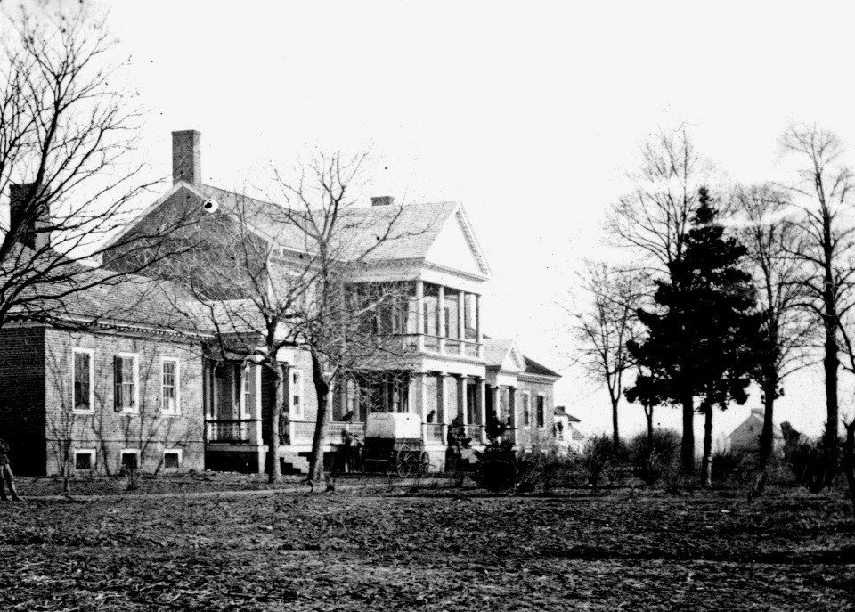 Black and white photo of large brick house with Civil War wagon and a number of trees in front