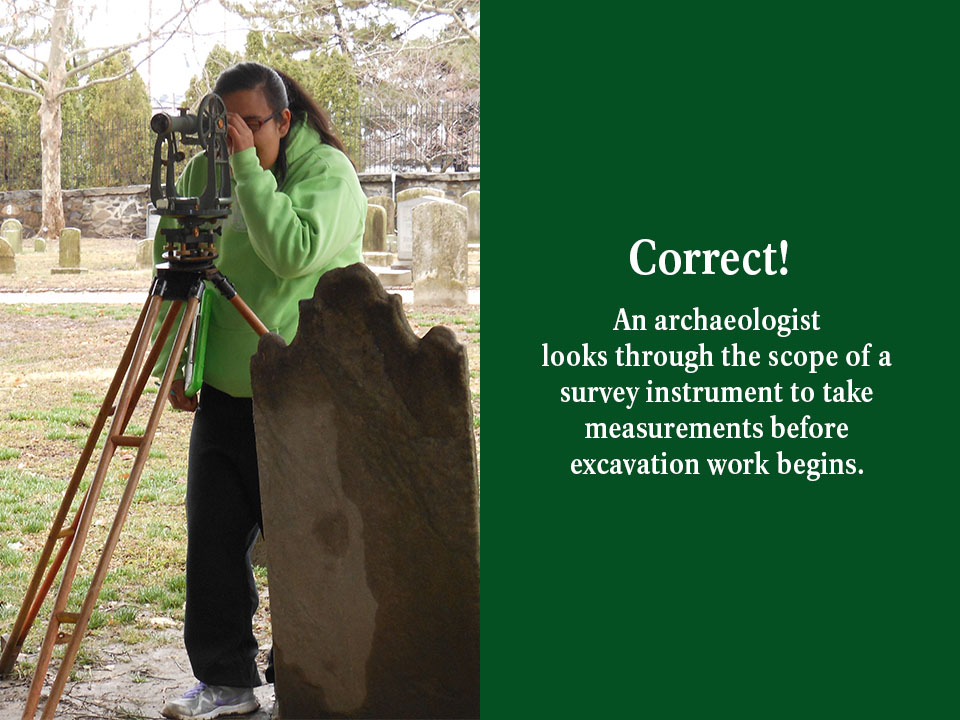 An archaeologist looks through the scope of a survey instrument to take measurements before excavation work begins.