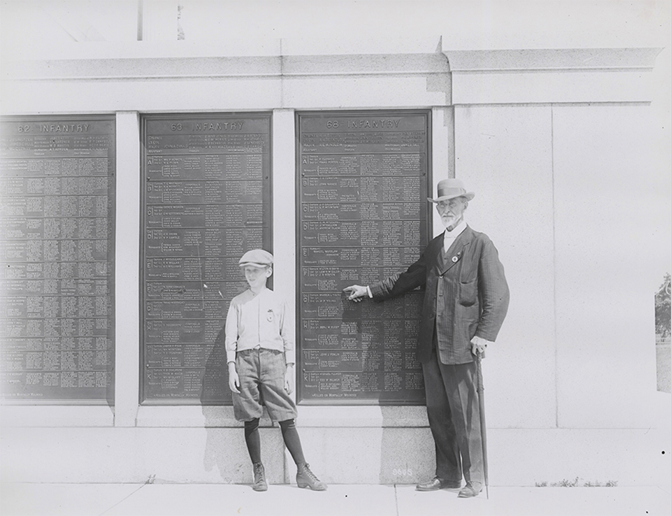 A Civil War veteran points to his name on a tablet on the Pennsylvania Memorial as a young boy looks on.