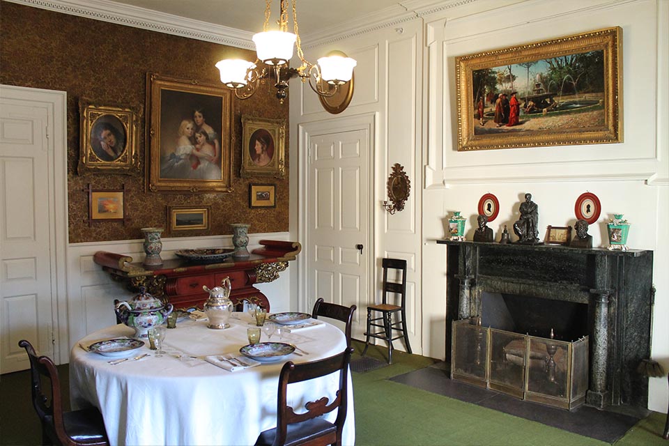 Black and white photograph of room with round table at center, paintings on walls