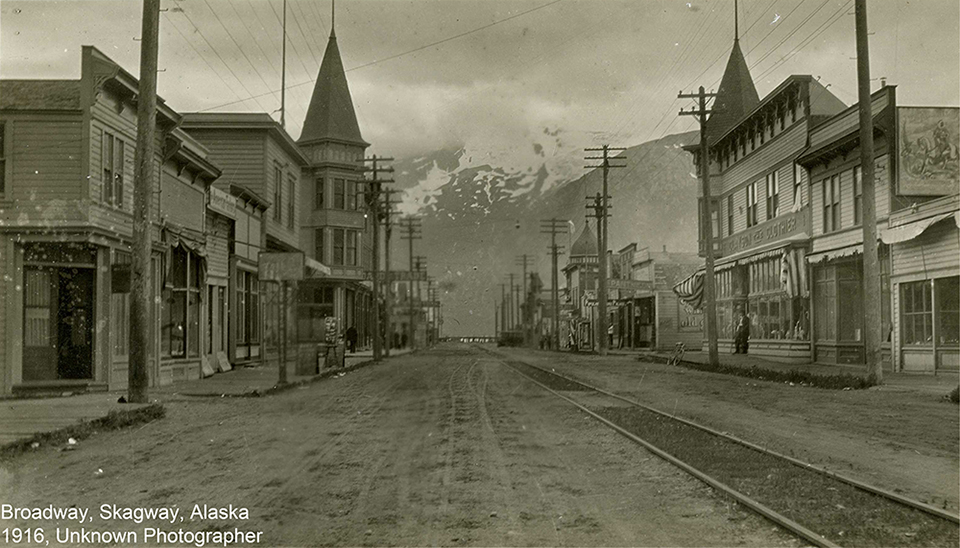 Black and white photo looking down a street towards mountains.