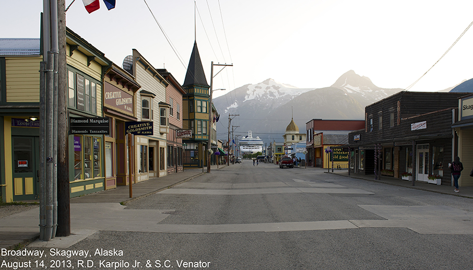 Black and white photo looking down a street towards mountains.