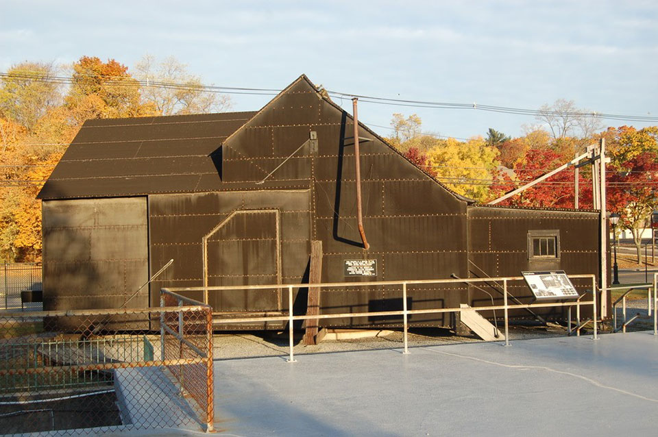 Three workers and a ladder stand at the front of a windowless building that is covered in black tar paper.