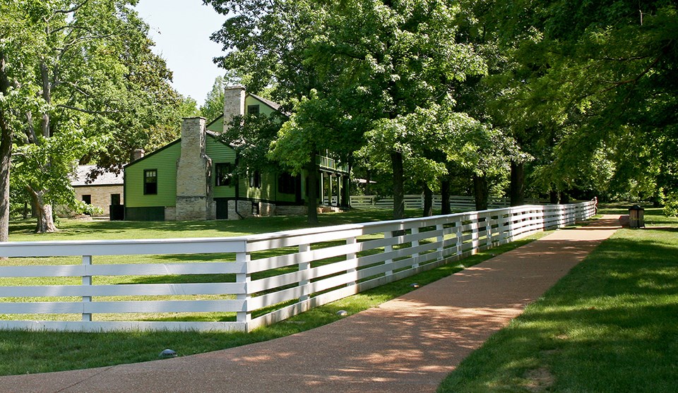 Black and white historic photo of a two-story house with a white rail fence