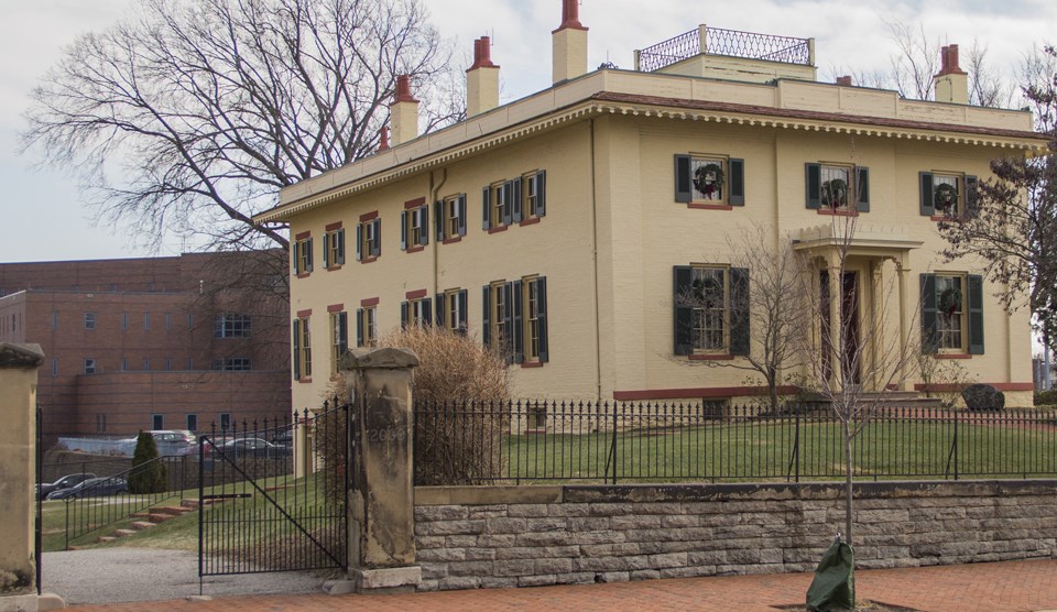 A large two-story home on a hill with several children pictured on the lawn and one child on a fence post