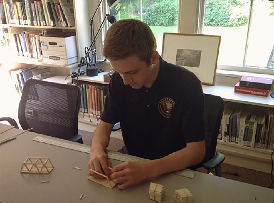 teenage boy building model bridge with popsicle sticks
