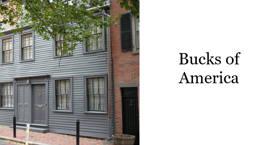 A greyish green clapboard house with two neighboring front doors for either unit of this duplex residence. One window is visible to the left of the doors, two are visible to the right.