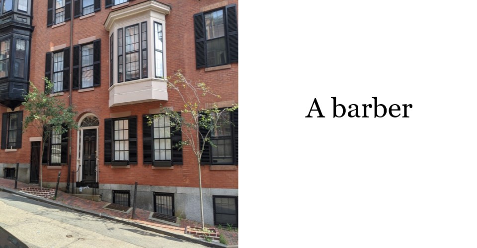 3 story brick row home on a sloped roadway where the right side of building basement is exposed and clad in granite. Middle second floor window is a white bay window protruding over sidewalk. All other windows are black shutters.