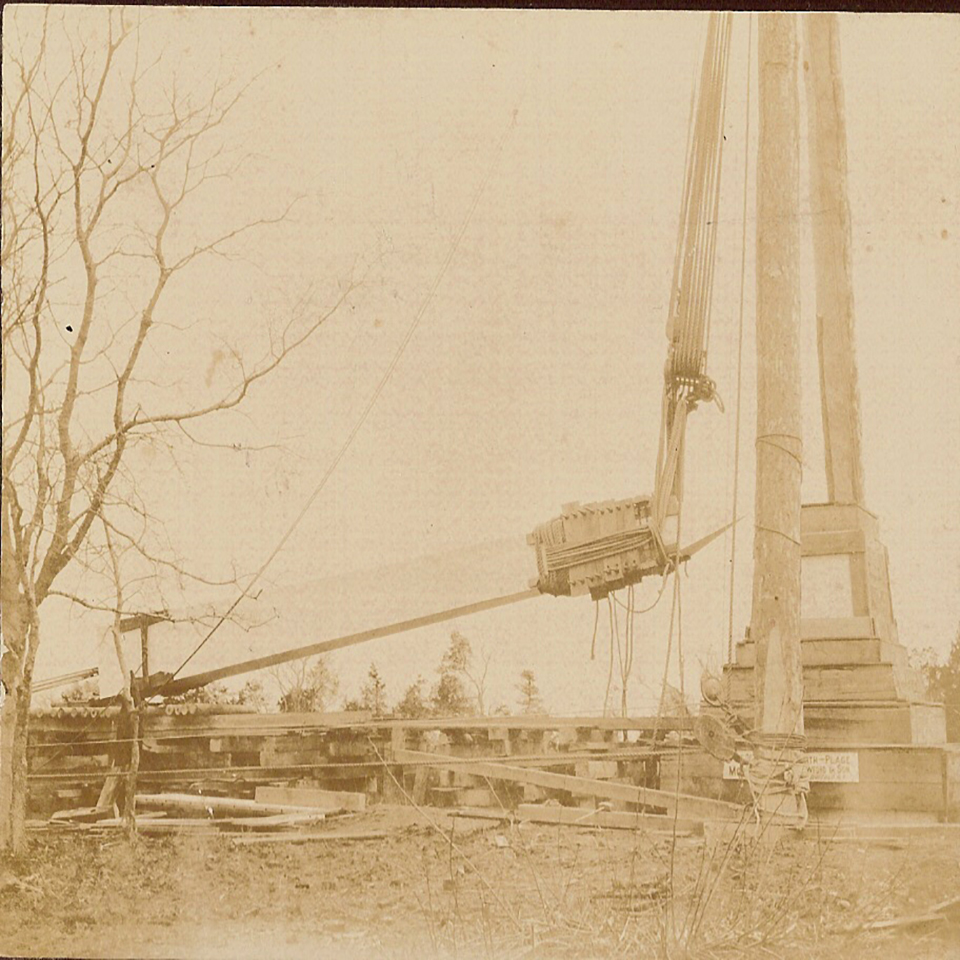 monument being lowered to greased logs by a pulley system attached to wooden derrick