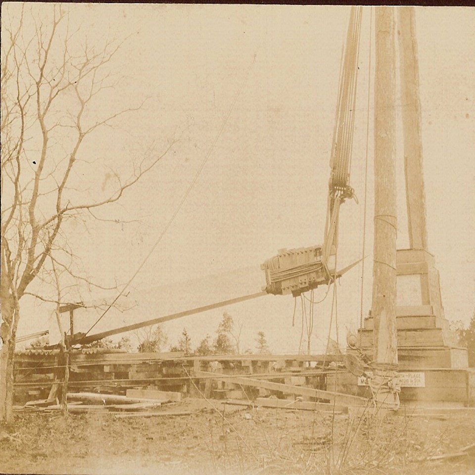 monument being lowered to greased logs by a pulley system attached to wooden derrick