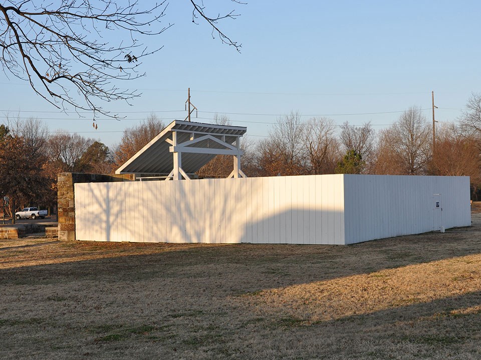 Tall white fence surrounds gallows only tip of slanted roof visible.