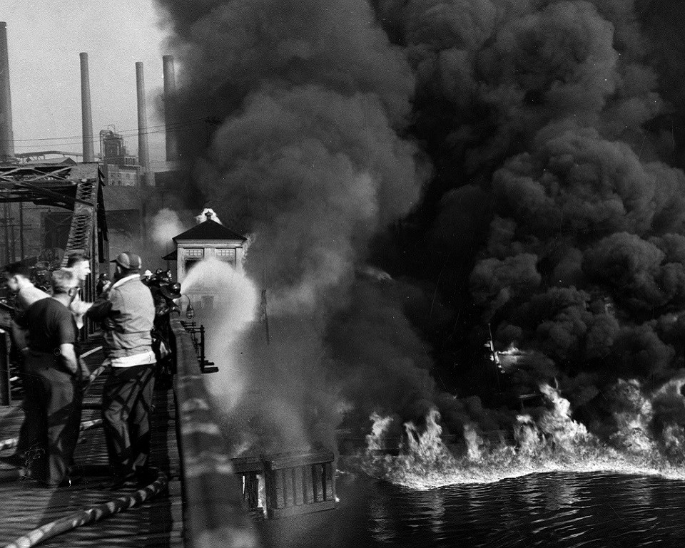 Black and white photo of firefighters fighting a fire on a river