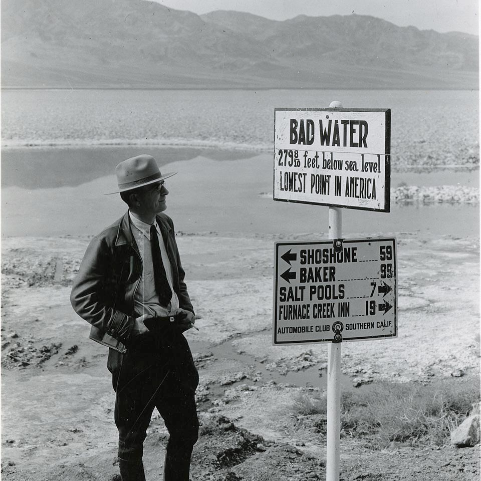A ranger in 1935 stands next to a sign that reads Badwater 279 feet below sea level