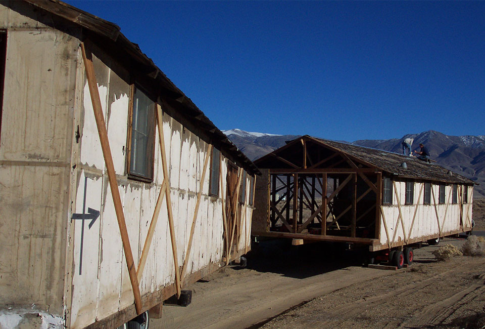 Two old run down barracks buildings being transported by trailer