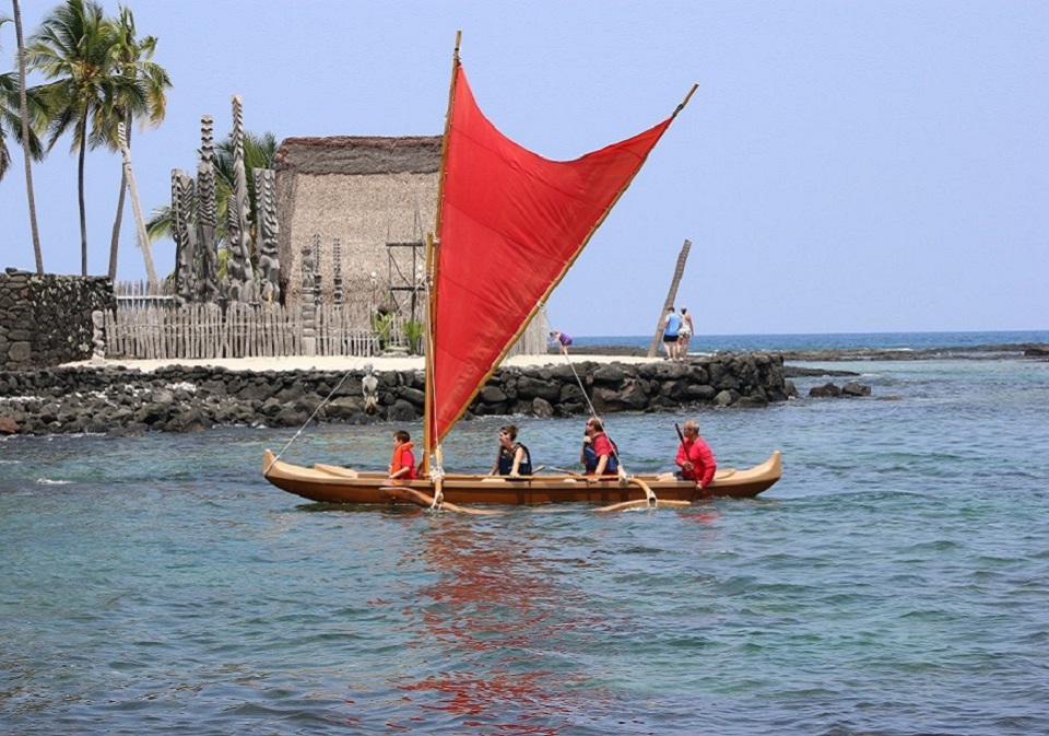 A historic photograph of a family enjoying a canoe ride in Keoneʻele Cove with Hale o Keawe in the background