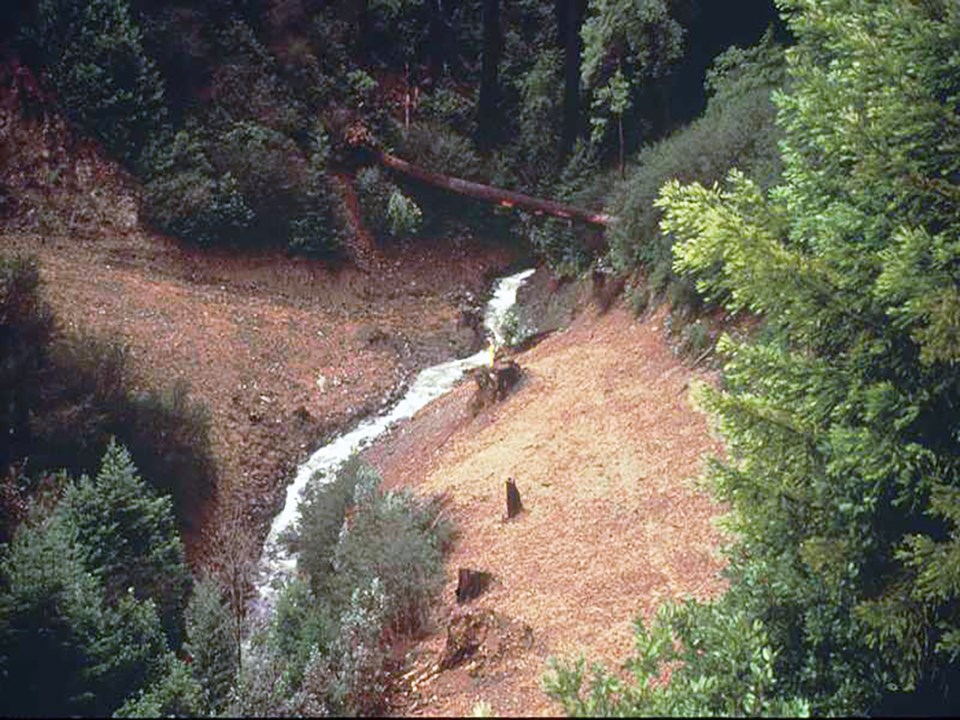A dirt road with heavy machinery on the left, with a culvert in the middle