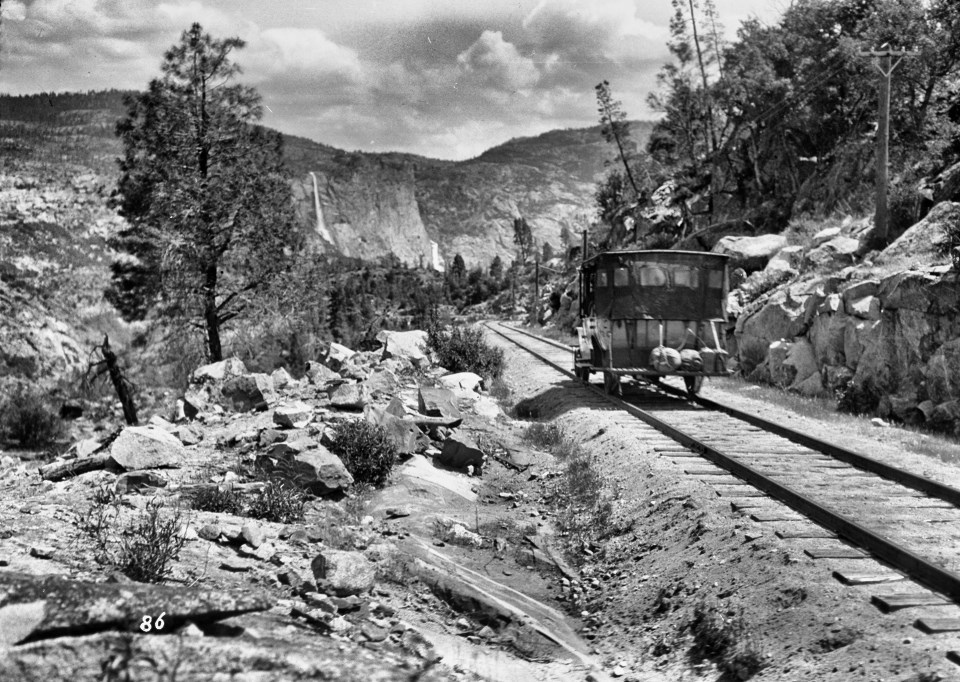 A car on railroad tracks with mountains and trees in background.